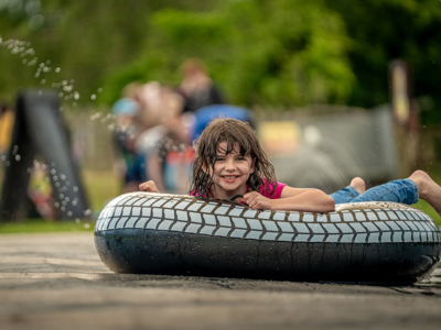 An image of a girl smiling as she zooms down a water slide on an inflatable doughnut.