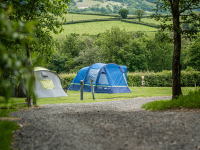 An image of two tents pitched on luscious green grass, with a wonderful view of Brecon all around.